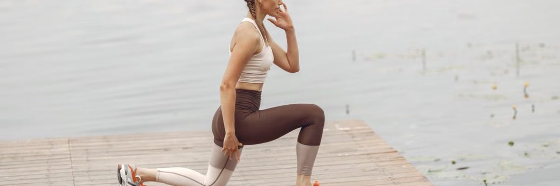A woman performs lunges on a lakeside wooden deck, showcasing a fit lifestyle outdoors.